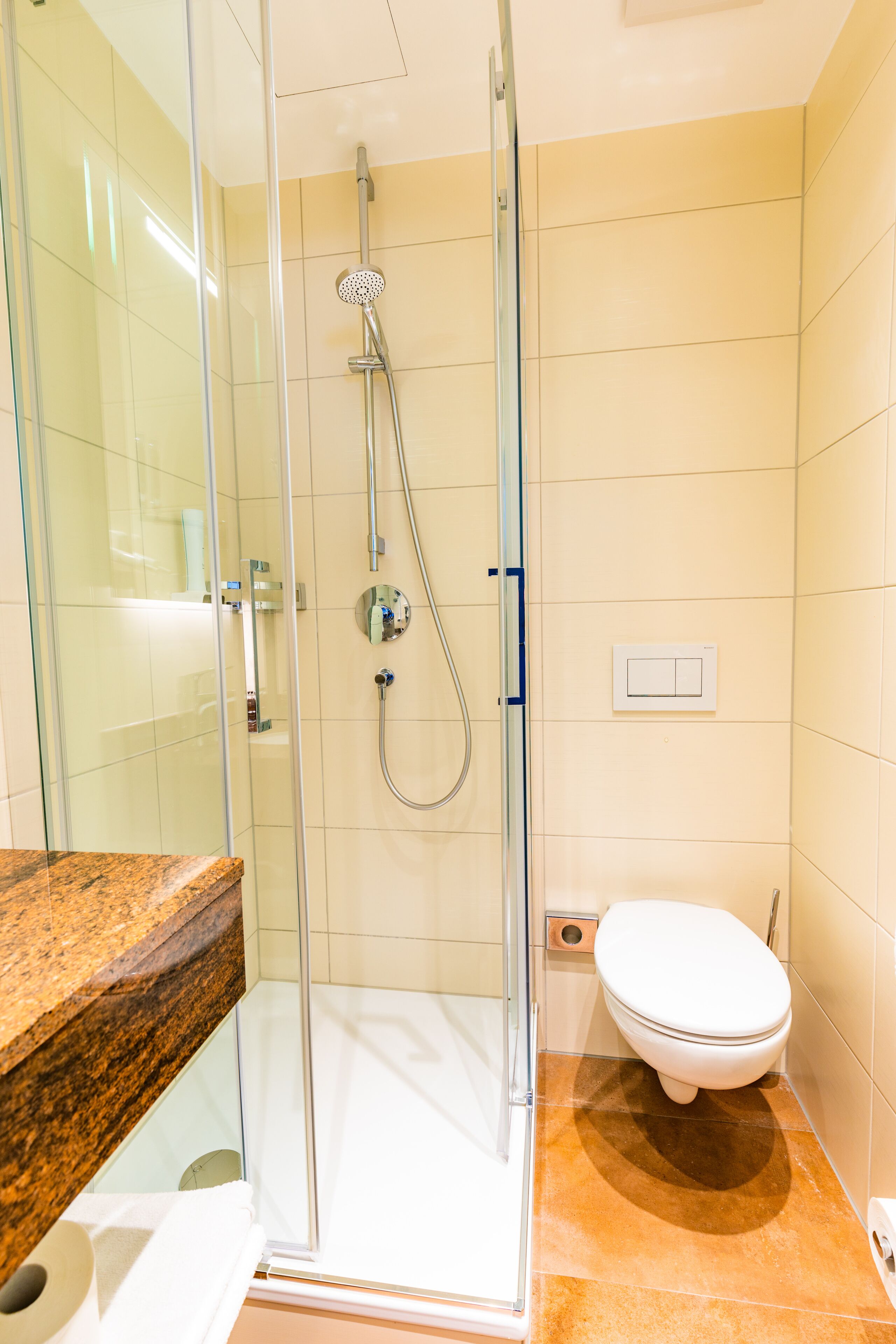 Een moderne badkamer met een douchecabine van glas, een wit toilet en een granieten aanrecht.