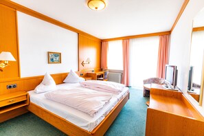 Une chambre d’hôtel avec un lit en bois, un bureau, une chaise, une télévision et une fenêtre avec des rideaux.