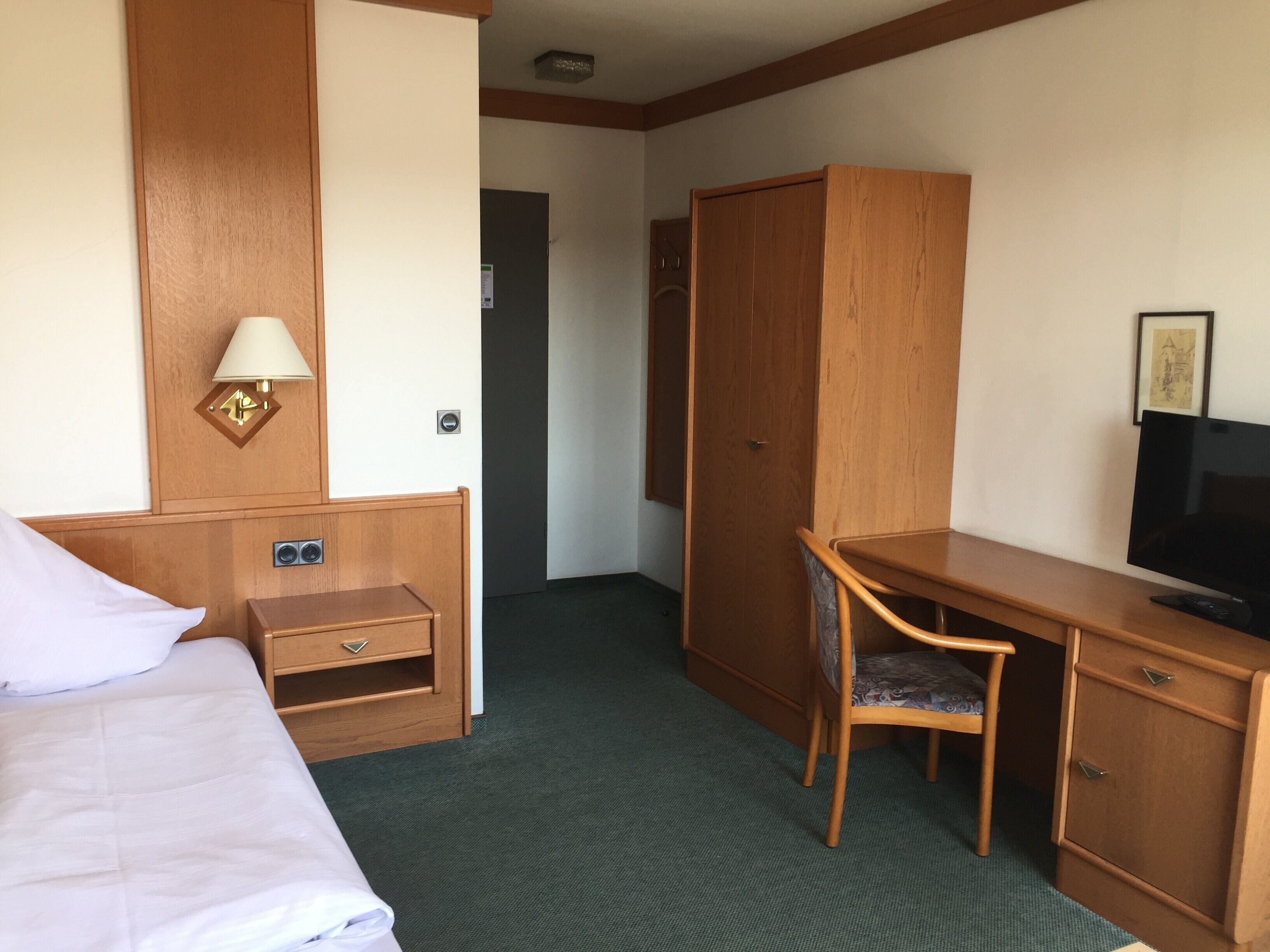 A hotel room with a bed, a desk, a chair, a television, and a wardrobe.