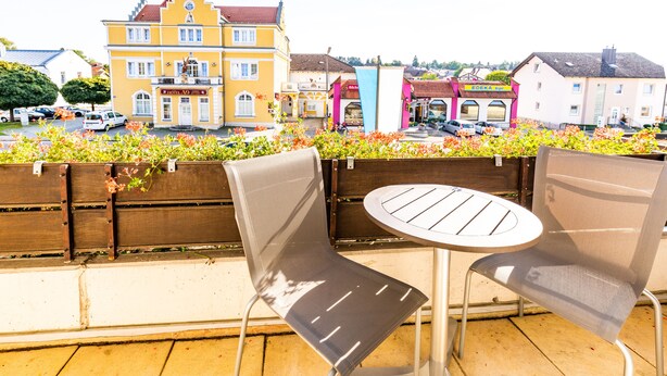 A balcony with two chairs and a table, overlooking a street with colorful buildings and parked cars. - Gasthof Pension Post (Denkendorf)