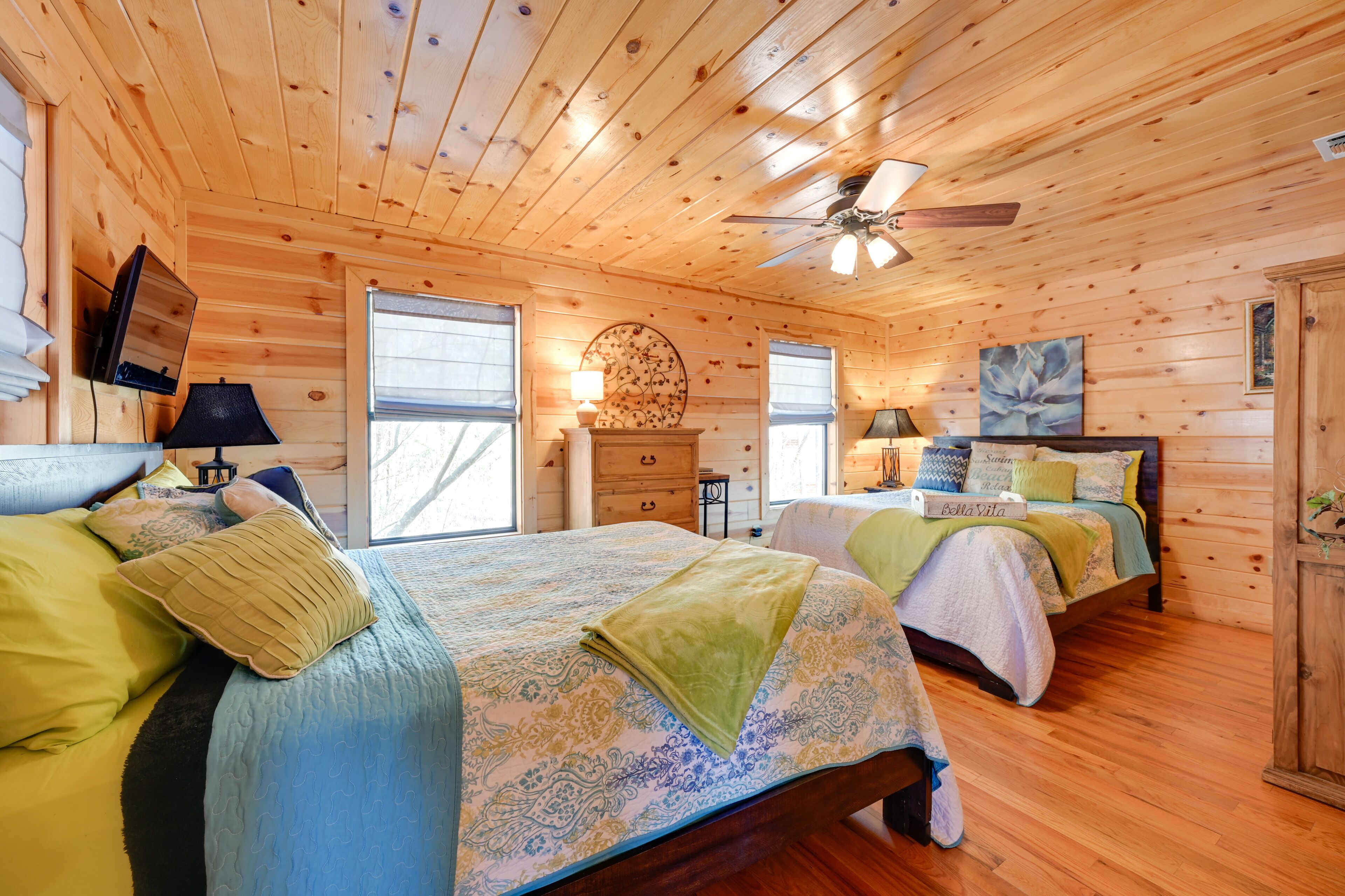 A wooden cabin bedroom with two beds, a ceiling fan, and a fireplace.
