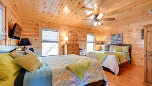 A wooden cabin bedroom with two beds, a ceiling fan, and a fireplace. - Broken Bow Cabin w/ Hot Tub & Fire Pit, Near Lake! (Broken Bow)