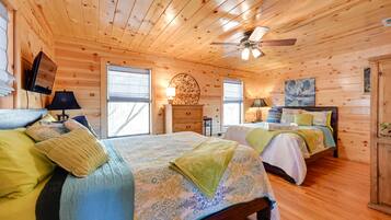 A wooden cabin bedroom with two beds, a ceiling fan, and a fireplace.