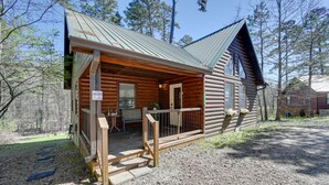A log cabin with a porch, a dining area, and a small outdoor seating space. - Broken Bow Cabin w/ Hot Tub & Fire Pit, Near Lake! (Broken Bow)