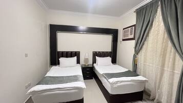 Habitación de hotel con dos camas individuales, una mesita de noche con lámpara, un espejo grande sobre las camas y una ventana con cortinas.
