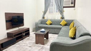 Un salón con un sofá gris, mueble de entretenimiento de madera y un televisor.