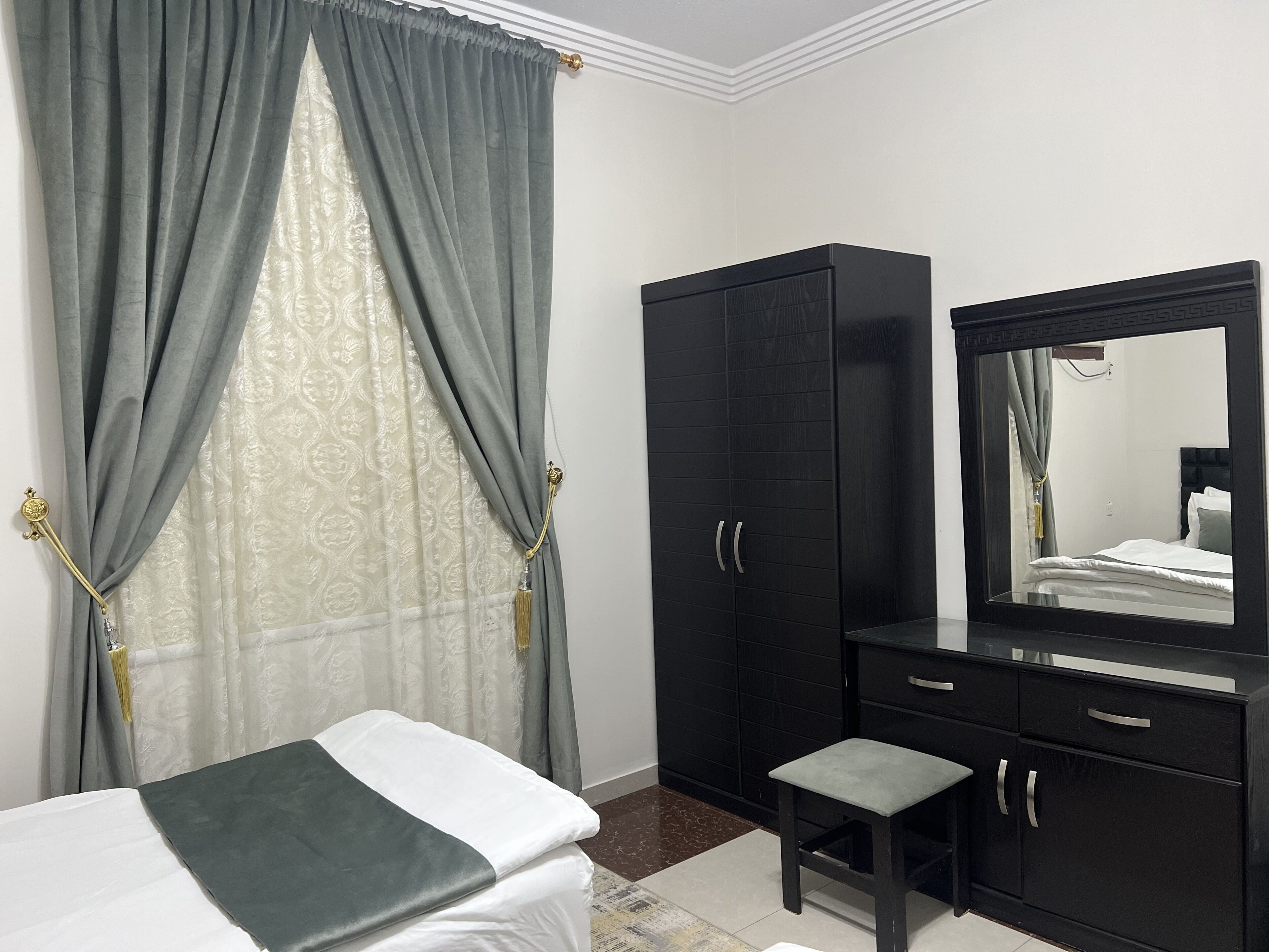 Un dormitorio con cama, armario, espejo y ventana con cortinas.
