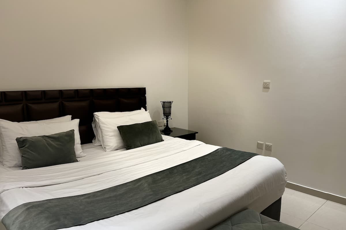 A neatly made bed with white and green bedding, a dark headboard, and a bedside table with a lamp.