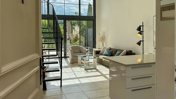 Un vaste espace de vie comprenant un escalier menant à un balcon, un canapé, une table basse et un coin cuisine avec un réfrigérateur.