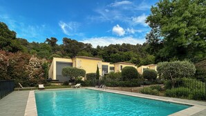 Une piscine dont le bord est revêtu de carrelage, entourée d’une clôture et de verdure.
