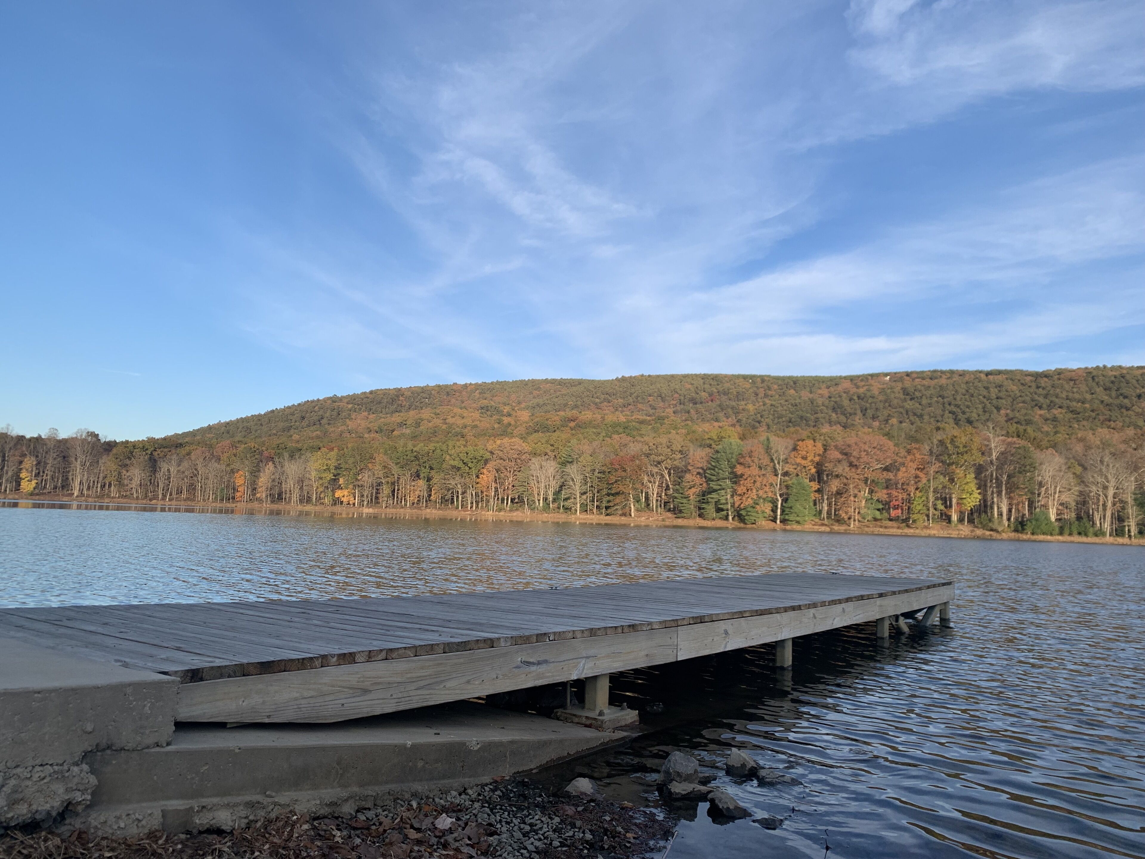 Eine hölzerne Mole, die sich in einen stillen See erstreckt, umgeben von Bäumen mit Herbstlaub.