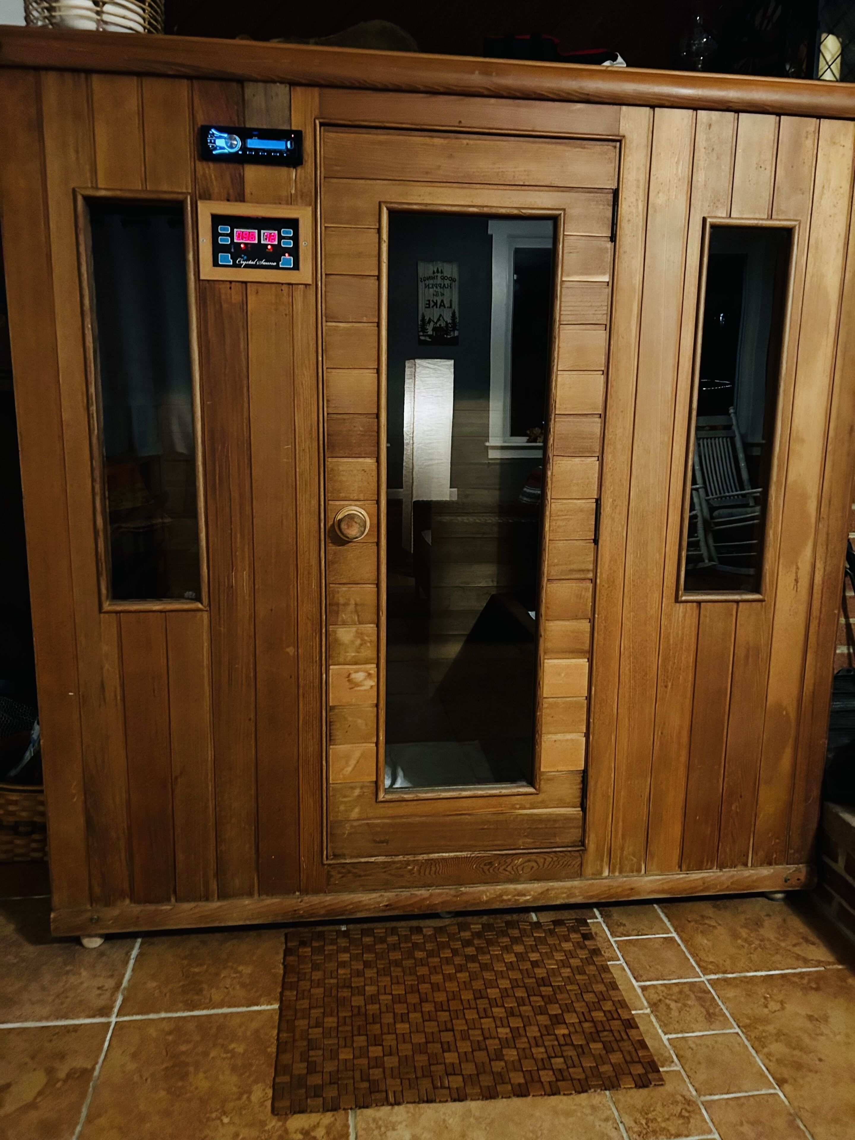 A wooden sauna with a digital control panel, a glass door, and a tiled floor.