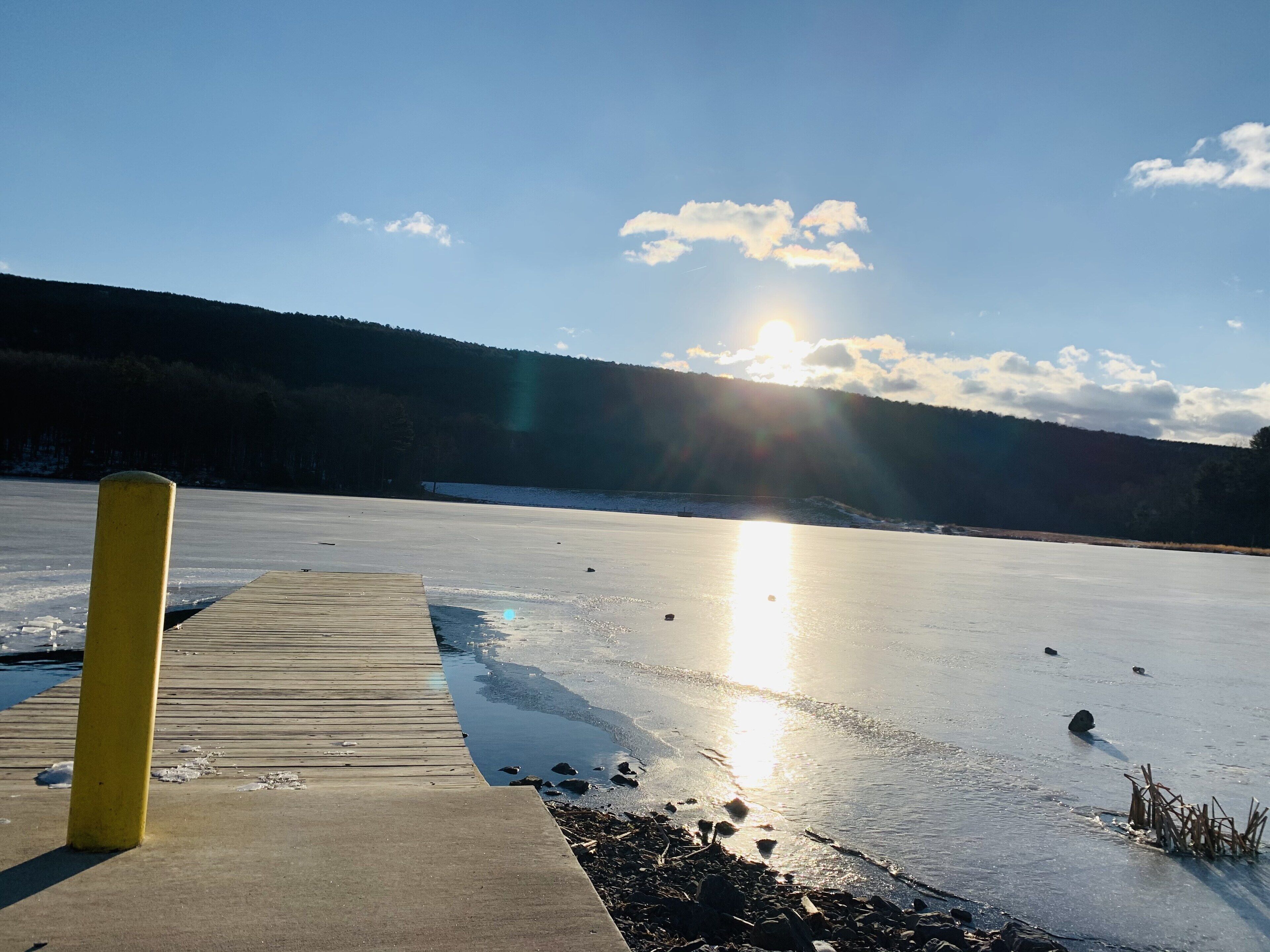 A frozen lake with a wooden dock extending into the water, surrounded by forested hills.
