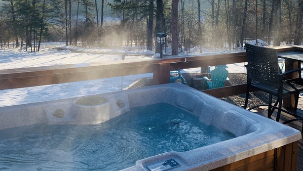 Een hottub omgeven door een houten terras, met sneeuw op de grond en bomen op de achtergrond.