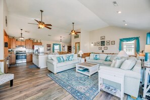 Ein geräumiger Wohnbereich mit Küche, zwei weiße Sofas mit blauen Kissen, einem Couchtisch und einem blau gemusterten Teppich.