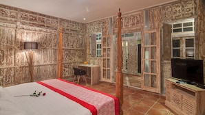 Ein Schlafzimmer mit einem Himmelbett, einem Schreibtisch mit Stuhl, einem Fernseher und einem großen Fenster.