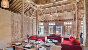 Ein geräumiger Essbereich mit einem Holztisch, gedeckt für eine Mahlzeit, umgeben von roten Sofas und weißen Stühlen.