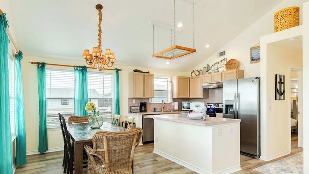 A modern kitchen with a central island, wooden flooring, and a dining area with wicker chairs. - Jamaica Beach Gem - Huge Deck, Fenced, Pups Welcome! (Jamaica Beach)