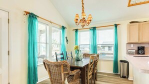 A dining area with a wooden table and wicker chairs, a chandelier, and teal curtains. - Jamaica Beach Gem - Huge Deck, Fenced, Pups Welcome! (Jamaica Beach)