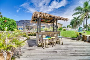 A wooden deck with a thatched roof structure, surrounded by lush greenery and palm trees. - Waterfront Merritt Island Vacation Rental w/ Pool! (Merritt Island)