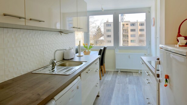 Una cocina moderna con armarios blancos, encimera de madera, lavavajillas integrado y ventana con vistas a la ciudad.