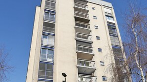 Un edificio alto de varios pisos con balcones, una farola y coches estacionados.