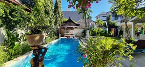 A swimming pool surrounded by lush greenery, a gazebo, and outdoor seating.