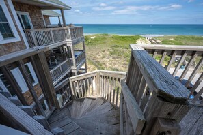 A wooden staircase leading to a balcony overlooking a beach with a clear view of the ocean.