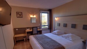 A hotel room with a bed, a desk, a chair, a mirror, and a window.