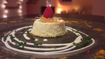A dessert with a raspberry on top, surrounded by white sauce and green garnish on a dark plate.
