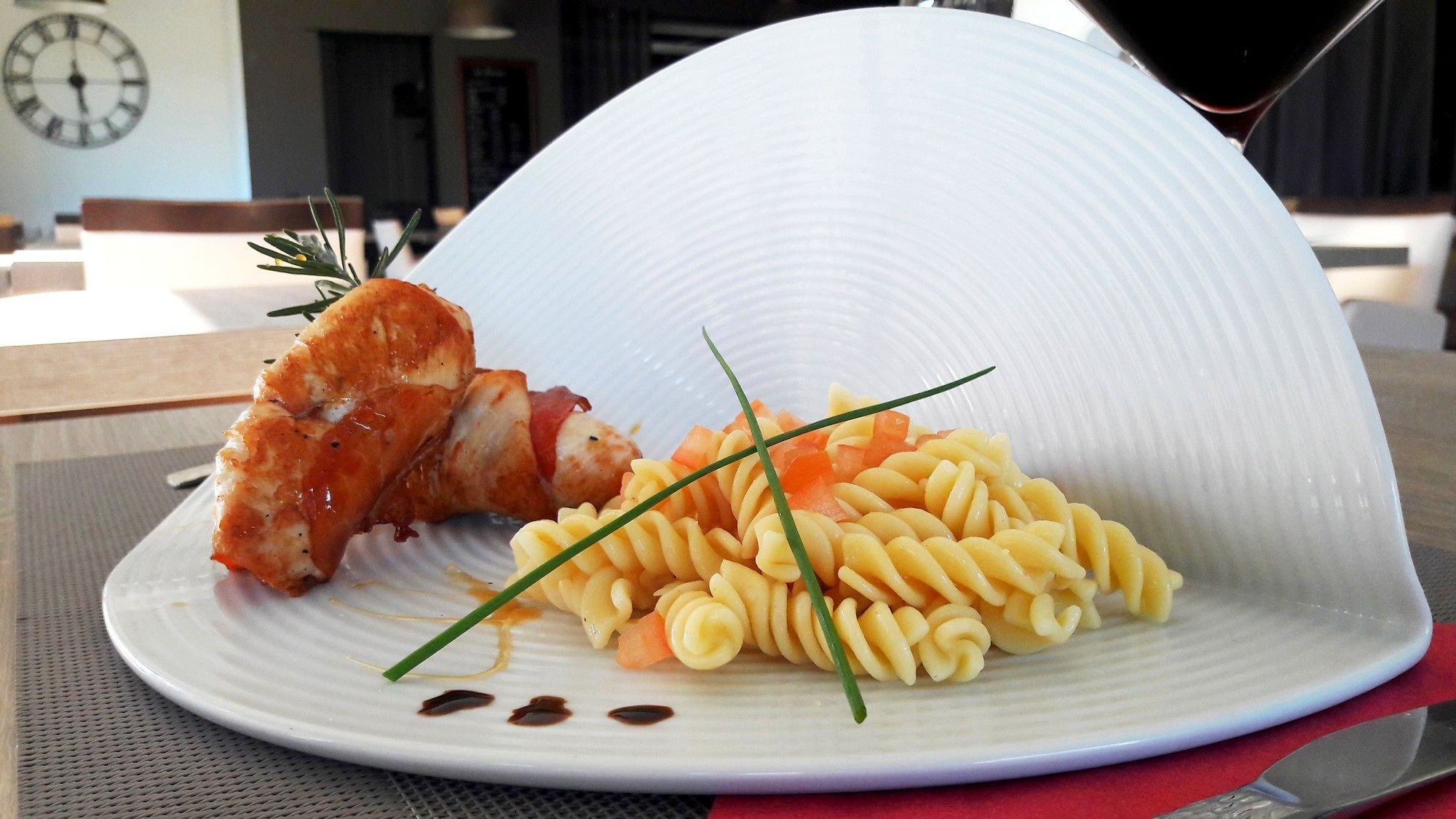 A plate with pasta, a piece of meat, and a garnish on a table.