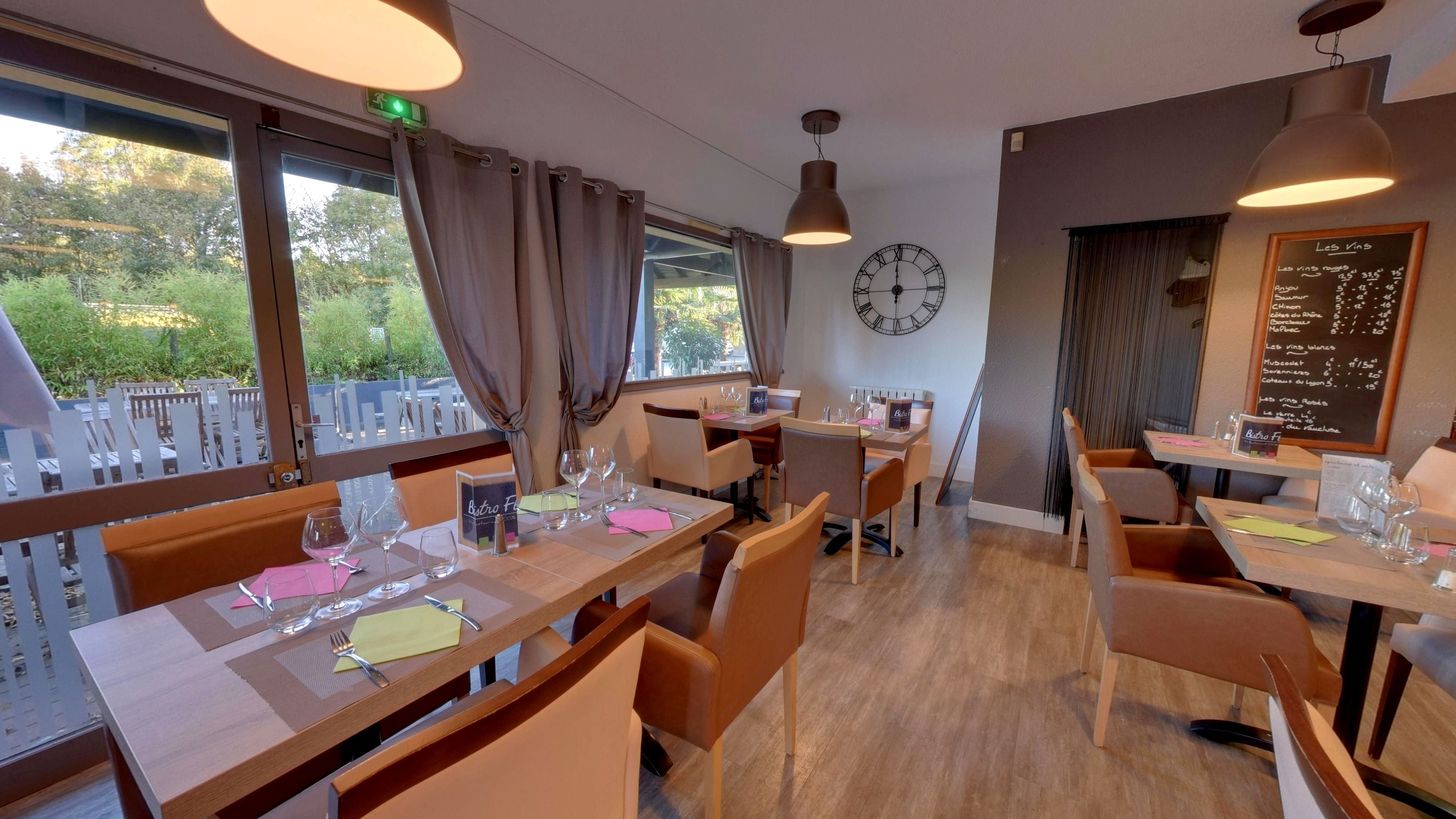A restaurant with tables set for dining, a clock on the wall, and a menu board.