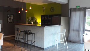 A modern kitchen with a bar area, bar stools, pendant lighting, and a green accent wall.