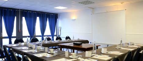 A conference room with long tables, chairs, nameplates, and a projector screen.