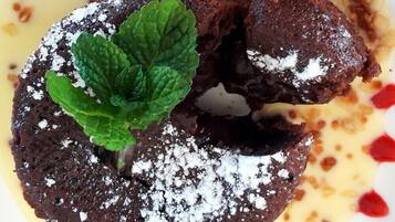 Un dessert composé d’un fondant au chocolat, de feuilles de menthe et de sucre glace, le tout servi sur une assiette avec une sauce crémeuse.