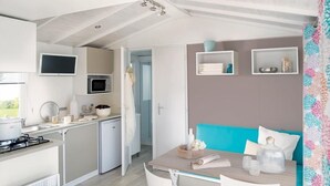 Et moderne køkken med mikrobølgeovn, komfur og vask. Der er spiseplads med et bord og stole, samt en blå sofa. Hylder med dekorative genstande sidder på væggen.