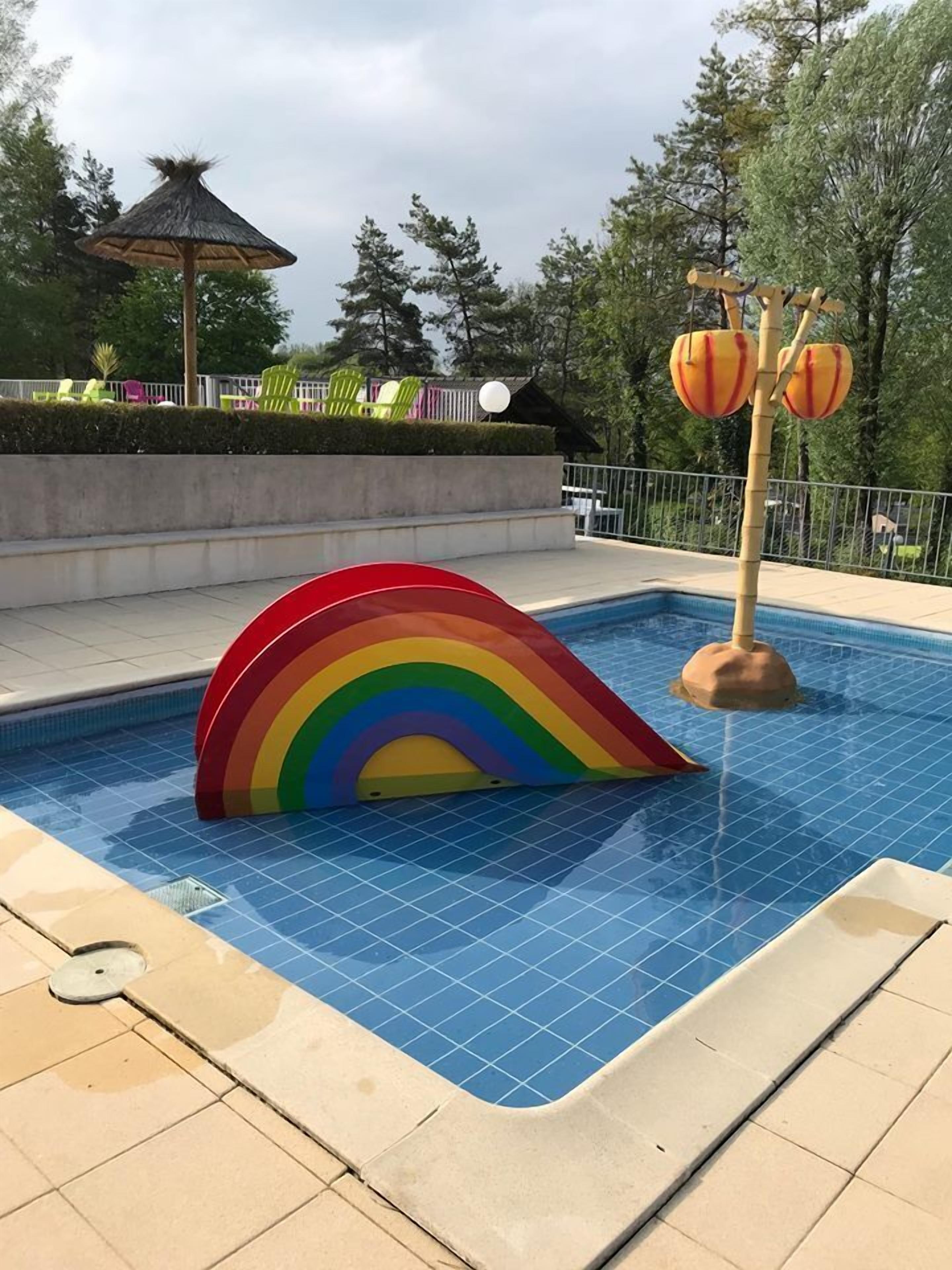 Ein Swimmingpool mit einer farbenfrohen Regenbogenstruktur und einer Springbrunnenanlage.