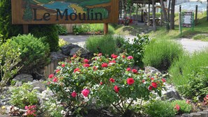 Et træskilt med teksten 'Le Moulin', omgivet af en have med røde blomster og grønt.