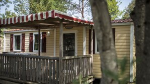 A wooden deck with a striped awning, a small porch, and a building with a red roof. - Camping Les Pêcheurs (Pont-de-Poitte)