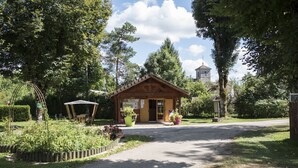 A rustic wooden building with a sloped roof, surrounded by lush greenery and a clear sky. - Camping Les Pêcheurs (Pont-de-Poitte)