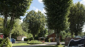 A residential area with a house, a covered patio, and a trailer. - Camping Les Pêcheurs (Pont-de-Poitte)