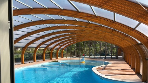 An indoor swimming pool with a wooden arched ceiling and clear glass panels. - Camping Les Pêcheurs (Pont-de-Poitte)