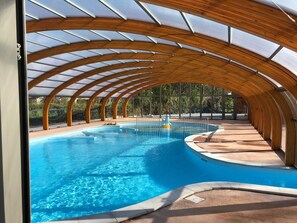 Piscina interior com teto abobadado em madeira e painéis de vidro transparente.
