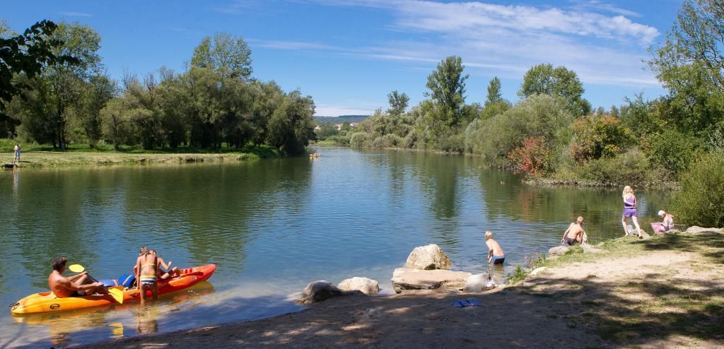 Ein ruhiger Fluss mit Leuten, die Kajak fahren und am Ufer stehen.