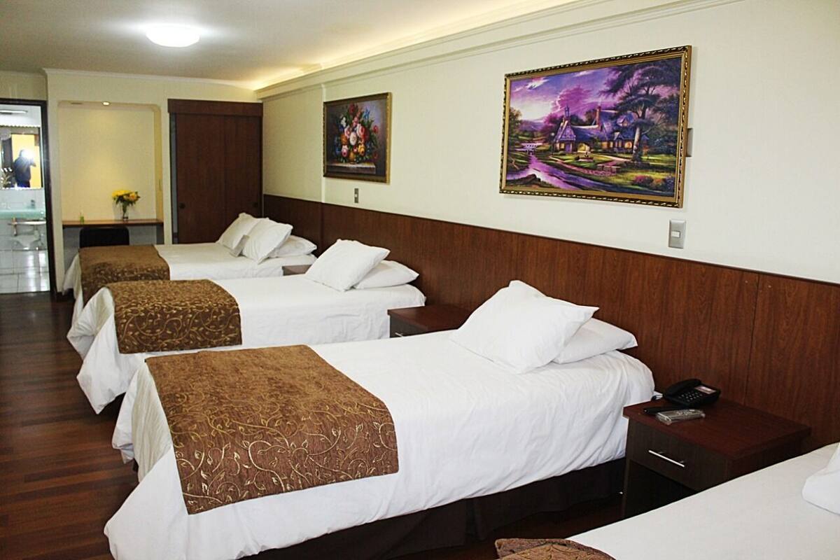 A hotel room with two beds, a wooden headboard, a bedside table with a phone, and artwork on the walls.