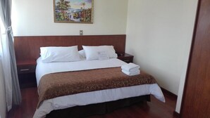 A neatly made bed with white and brown bedding, a nightstand with a lamp, and a painting on the wall. - Hotel Newen (Temuco)