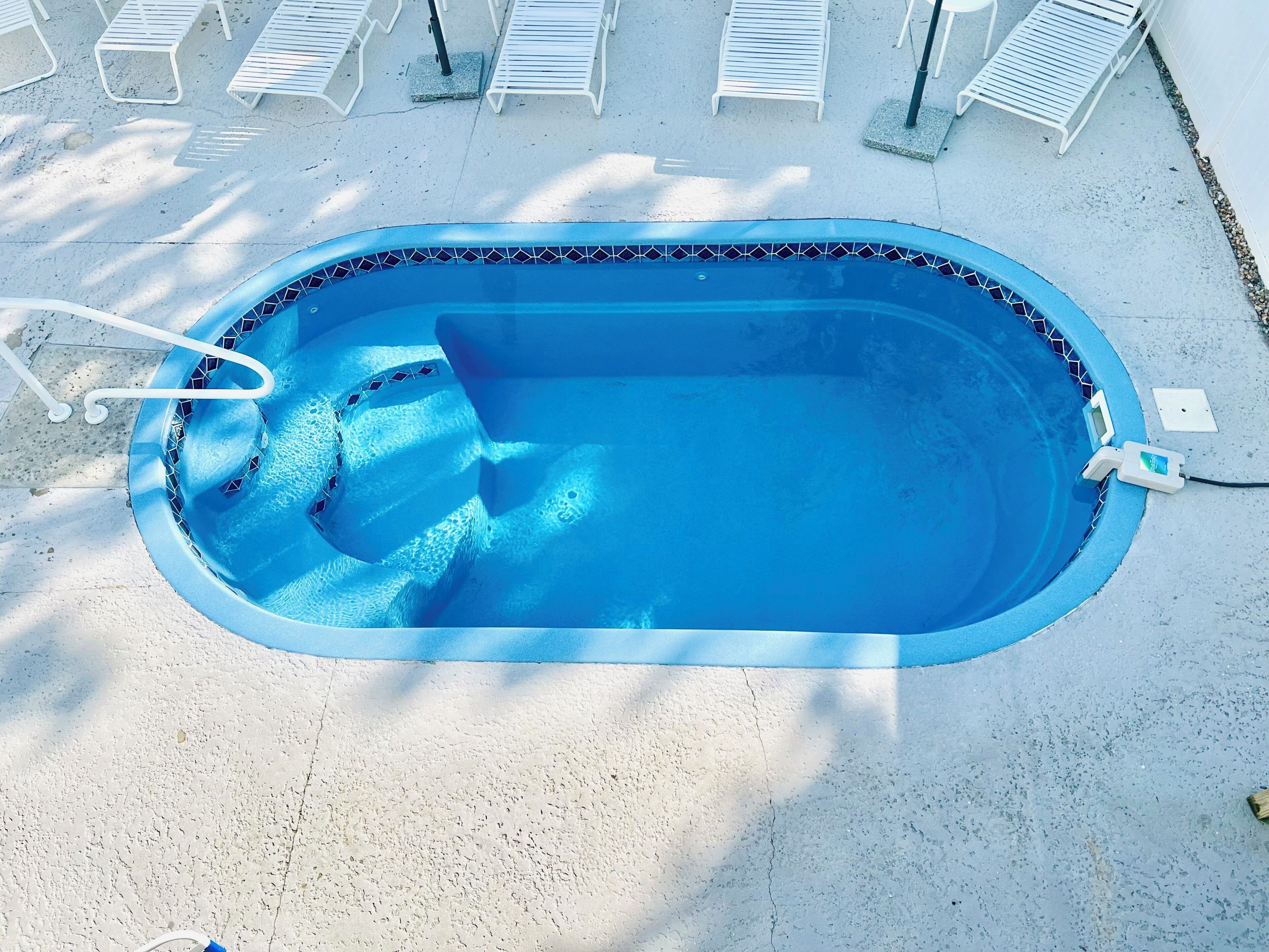 A swimming pool with a tiled edge, a ladder, and a poolside chair area.