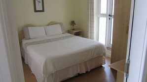A neatly made bed with a white duvet and pillows, a bedside table with a lamp, and a window with curtains. - Comfortable, Modern, Luxury, Secure, Beachfront, Seafront, City Centre (Galway)