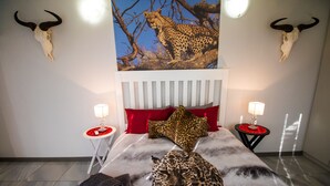Een slaapkamer met een laken met luipaardprint, twee schedels aan de muur en een kussen met luipaardprint.