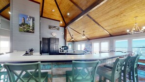 Une cuisine spacieuse dotée d’un grand îlot central, de poutres apparentes en bois et offrant une vue sur l’extérieur.